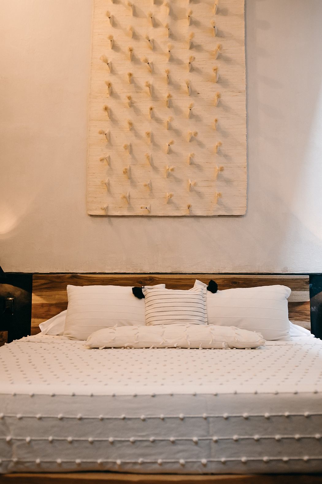 A modern bedroom with a wooden headboard, white bedding, and an abstract art piece on the wall.