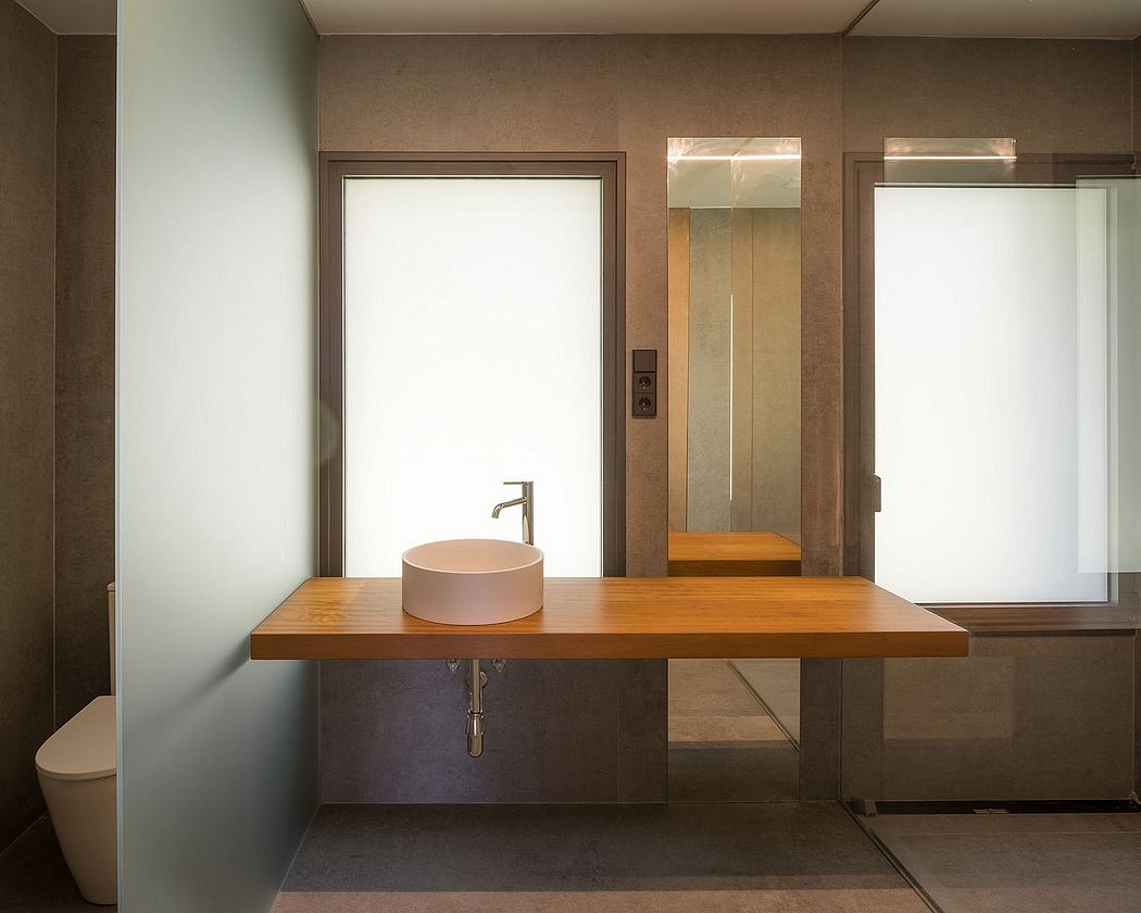 A modern bathroom interior with a wood vanity, round sink, and mirror-framed wall.