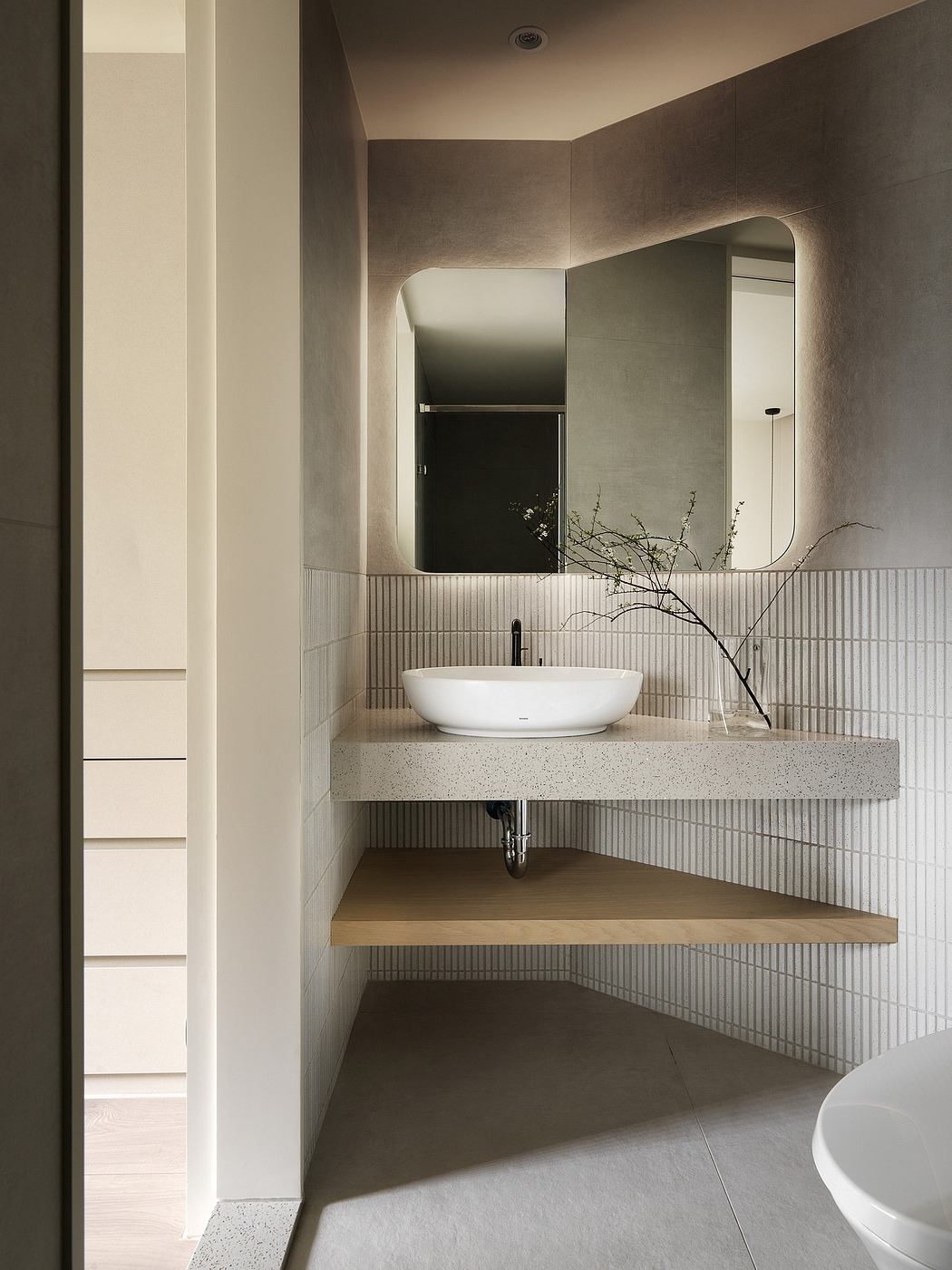 A minimalist bathroom with a modern oval sink, illuminated mirror, and shelving.