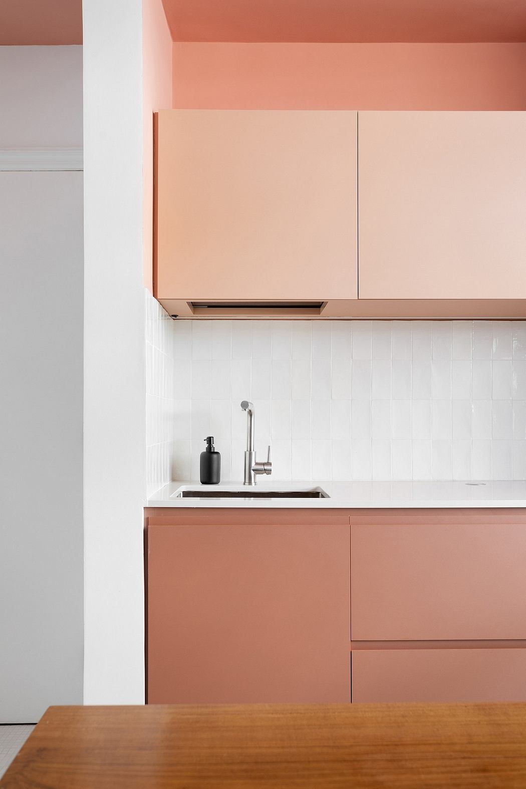 A modern kitchen design featuring peach-colored cabinets, a stainless steel sink, and a wooden table.