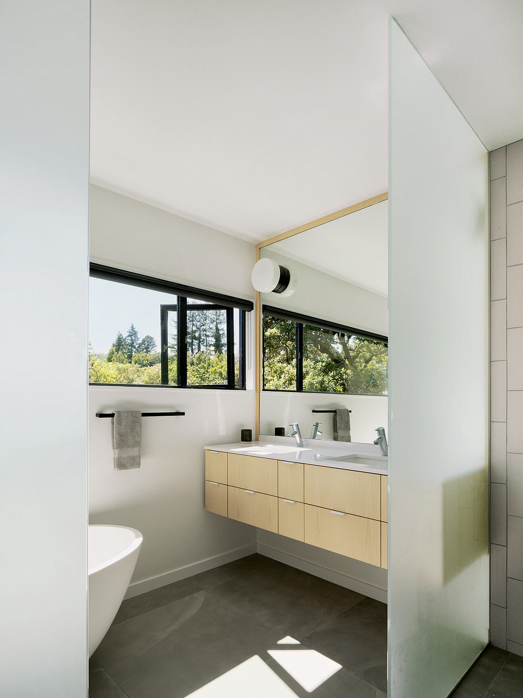 Bright, minimal bathroom with large windows overlooking lush greenery outside.