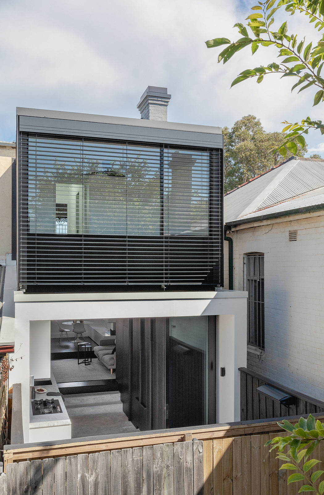 A modern, minimalist home with sleek glass walls, a balcony, and a chimney stack.