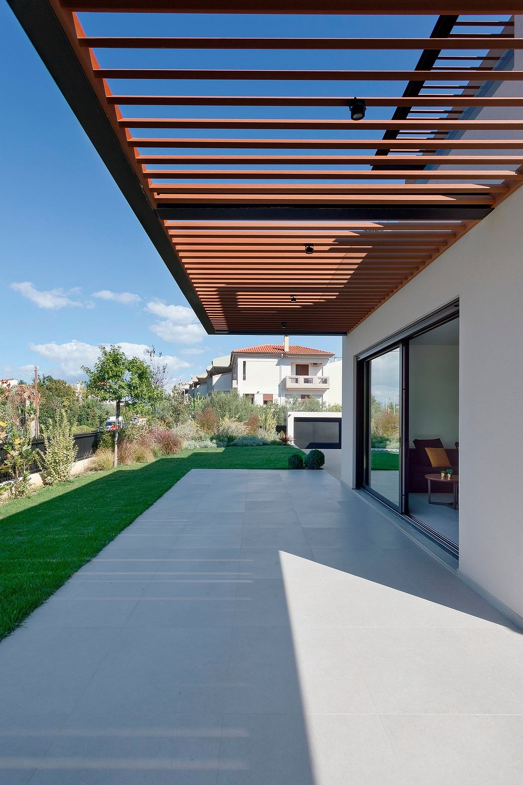 A modern outdoor patio with a wooden pergola overhead, a lush green lawn, and sliding glass doors.