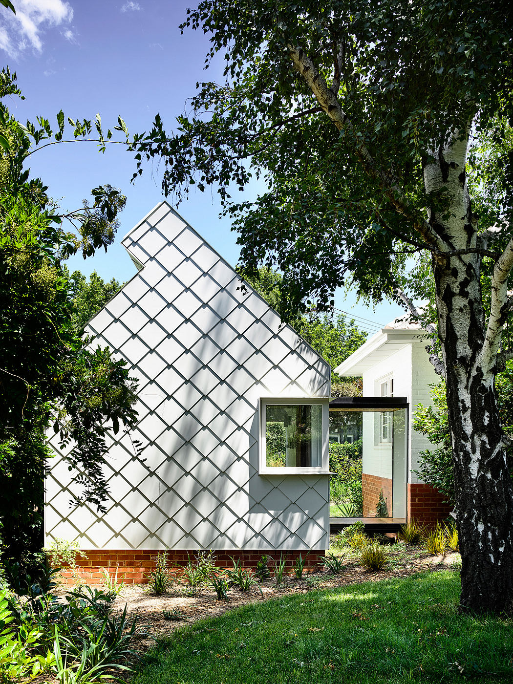 A modern, angular greenhouse-like structure with a striking glass facade nestled among lush greenery.