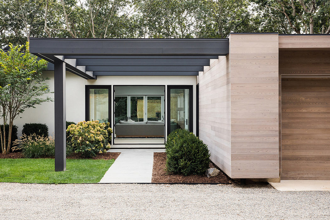 Modern, minimalist home with clean lines, neutral tones, and glass entryway surrounded by lush greenery.