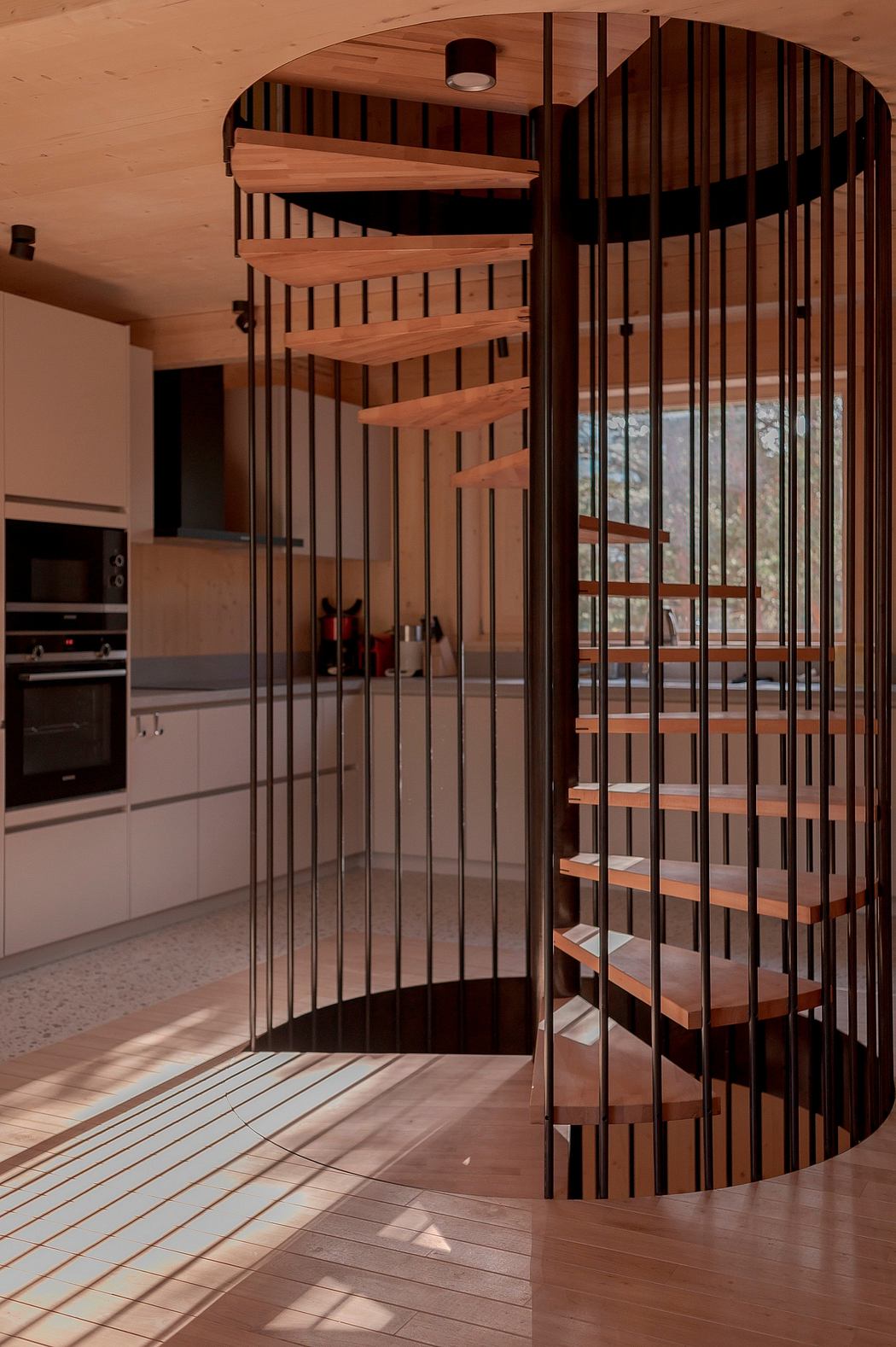 A spiral staircase with intricate wooden slat railings leads to an open kitchen area.