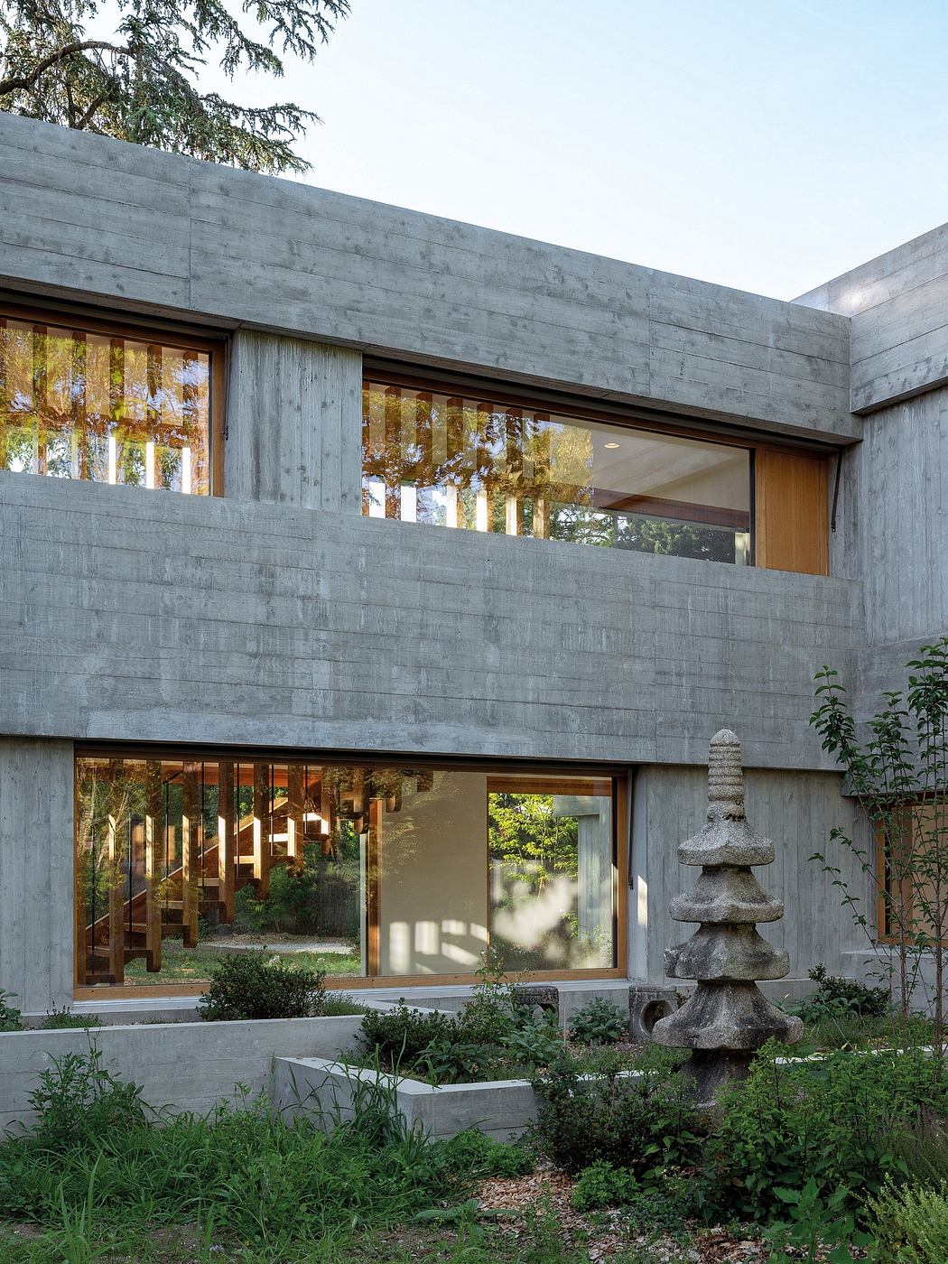Striking modern architecture with concrete walls and large glass windows framed by greenery.