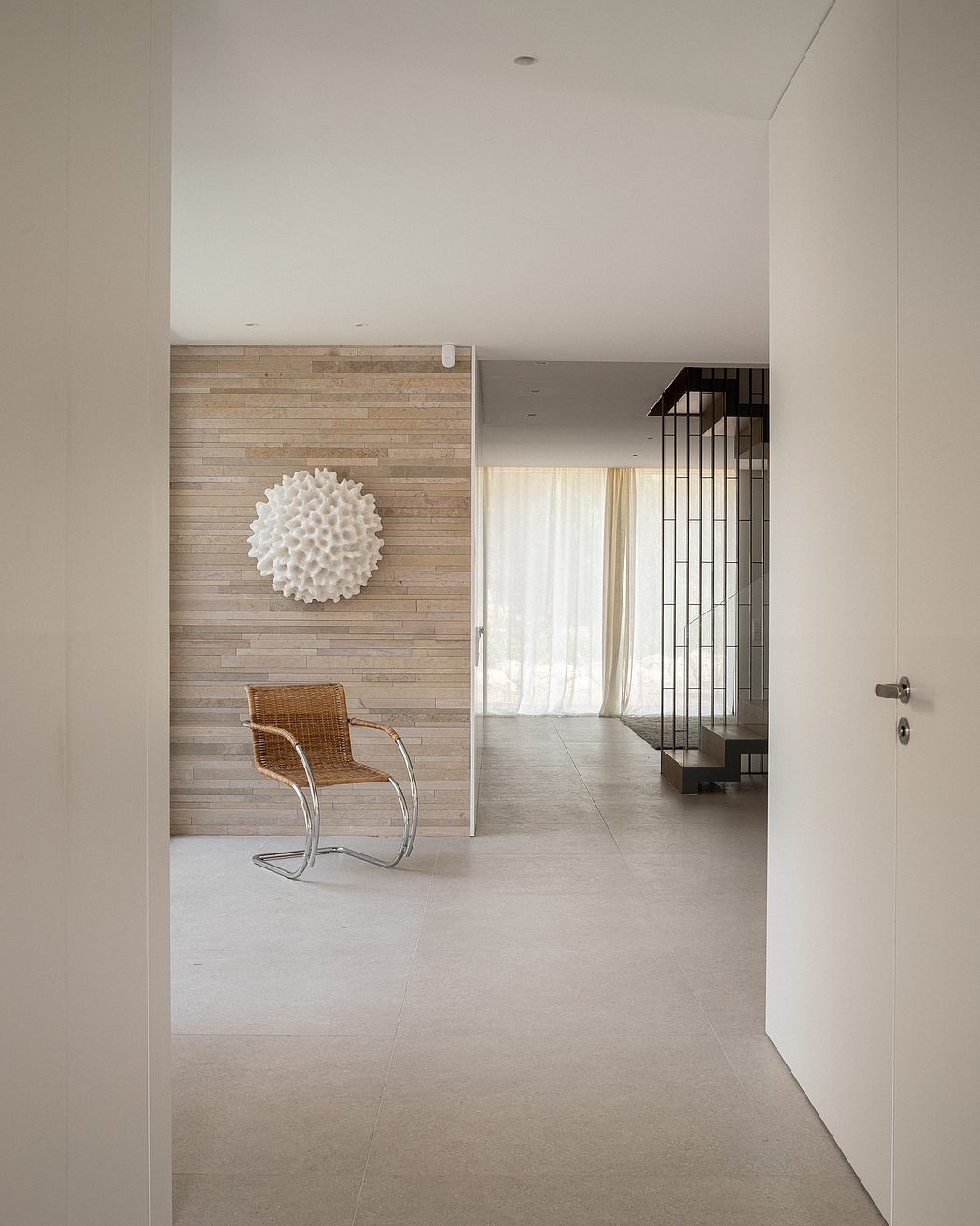 Minimalist entryway with textured stone wall, wicker chair, and geometric metal divider.