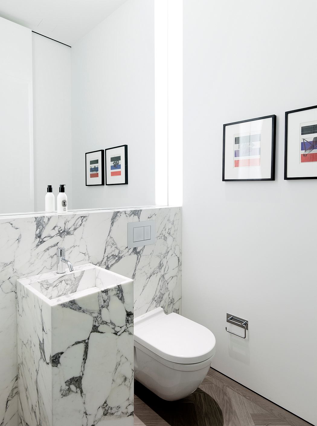 Minimalist bathroom with white walls, marble vanity, and framed abstract artwork.