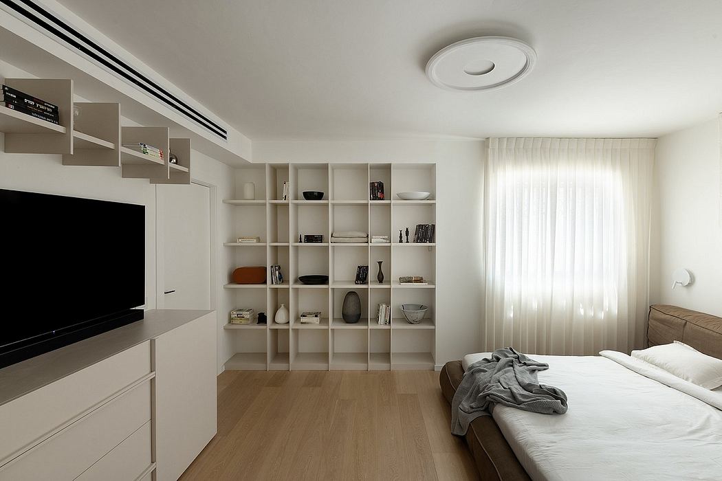 Minimalist bedroom design with built-in shelving, TV, and natural light from window.