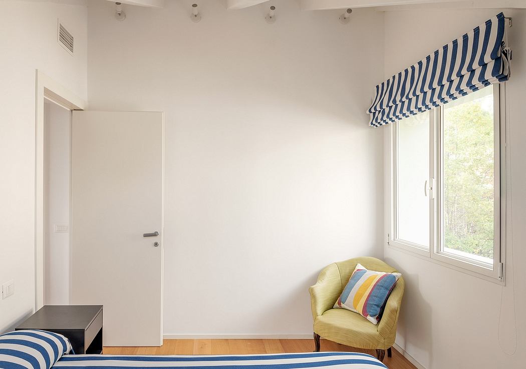 A simple, minimalist bedroom with a striped window treatment and a cozy armchair.