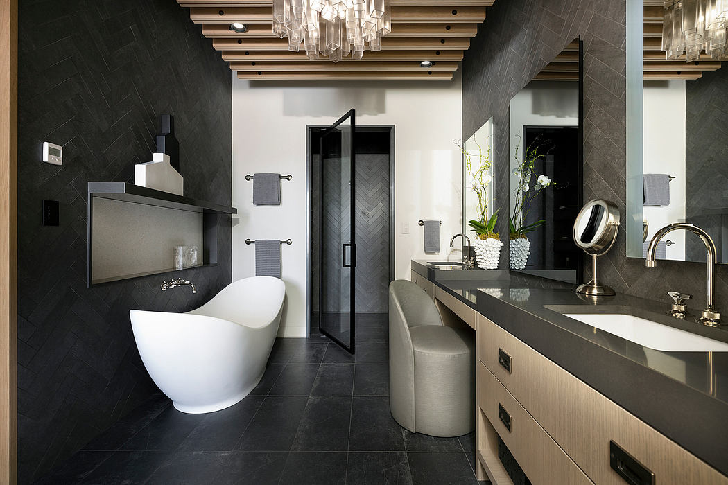 Luxurious bathroom with dark tile, freestanding tub, vanity, and ornate chandelier.