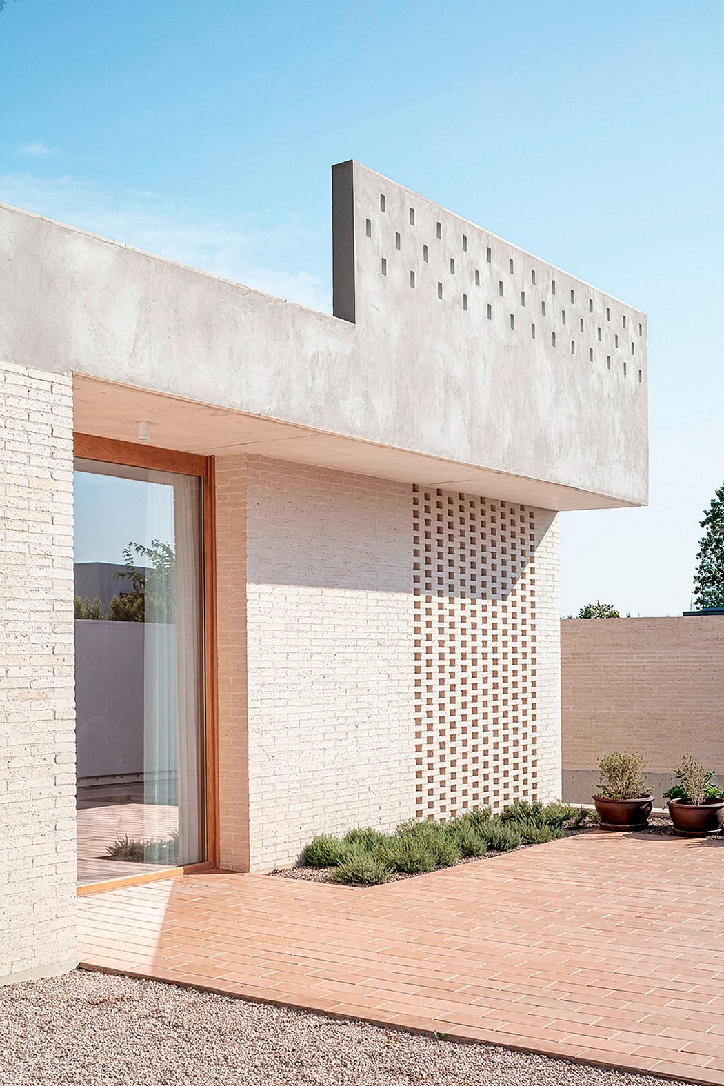 Modern architectural exterior featuring a brickwork facade, raised wooden deck, and potted plants.