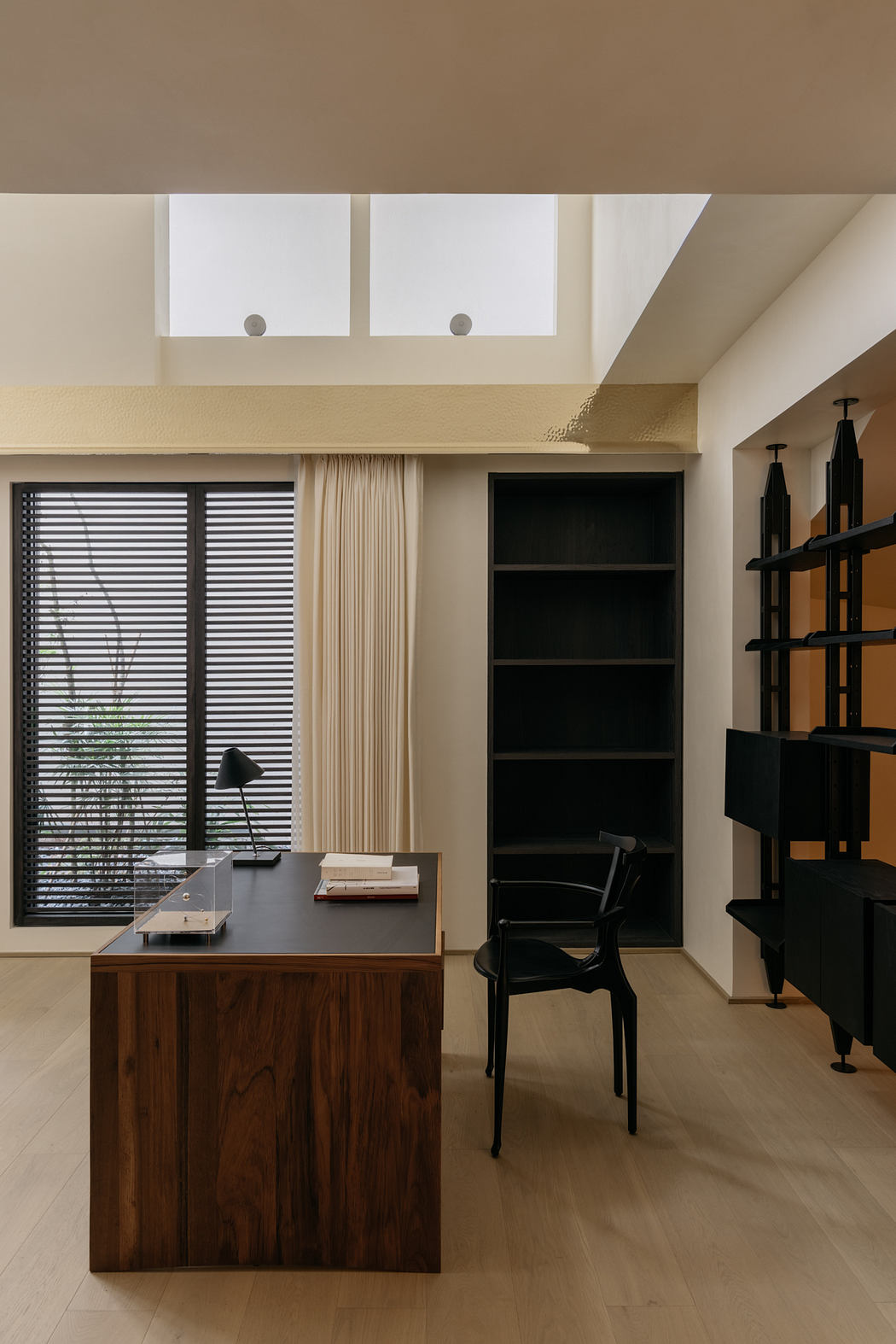 Modern home office with sleek wood desk, black chair, and recessed shelving.