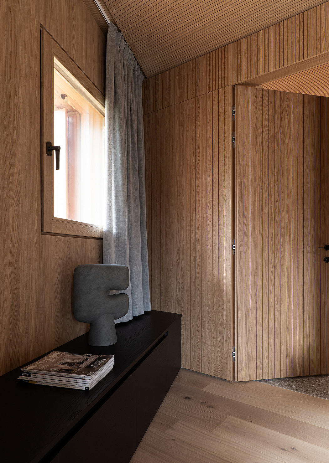 Warm, wooden interiors with minimalist furnishings and a window overlooking the outdoors.