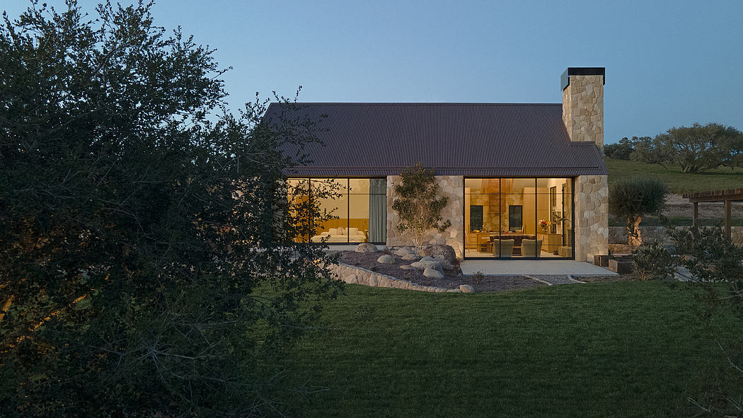 A modern stone and wood-paneled home with a large porch and stone chimney nestled among trees.