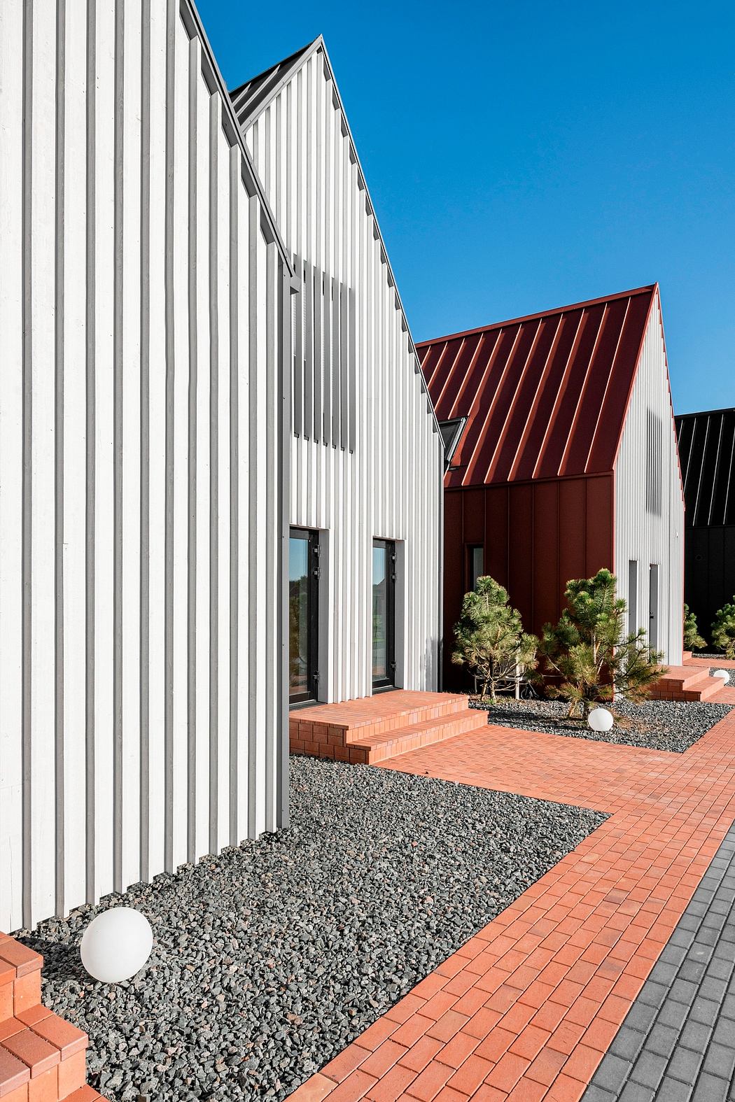 Modern architectural design featuring contrasting materials and textures, with a striking red-roofed building and a well-designed landscape.