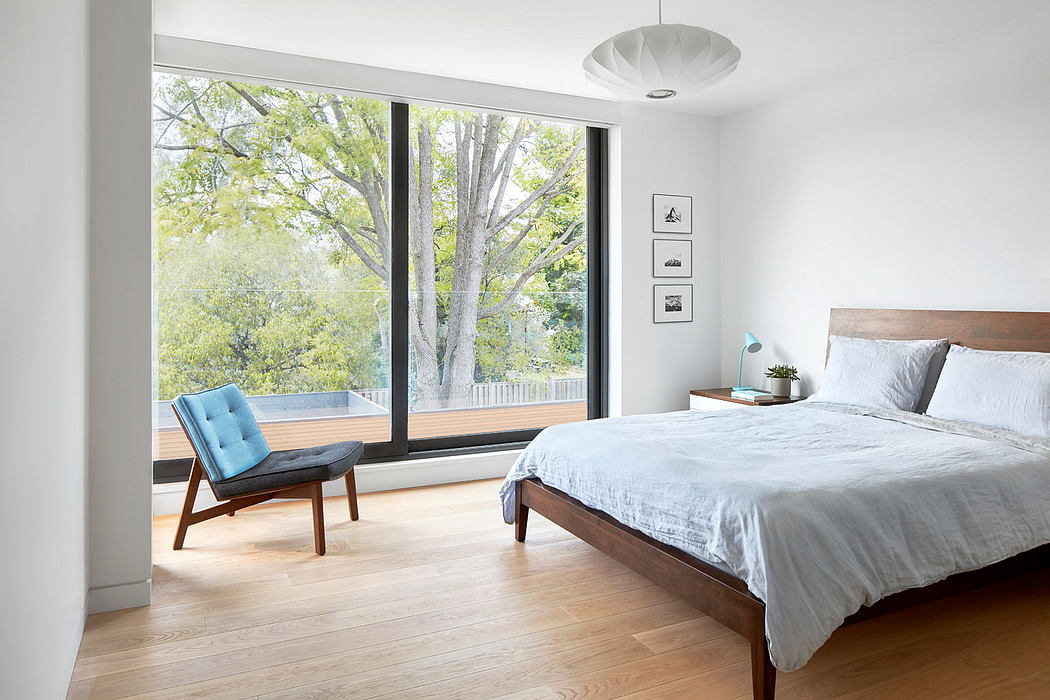 Minimalist bedroom with large windows overlooking lush greenery and a statement pendant light.