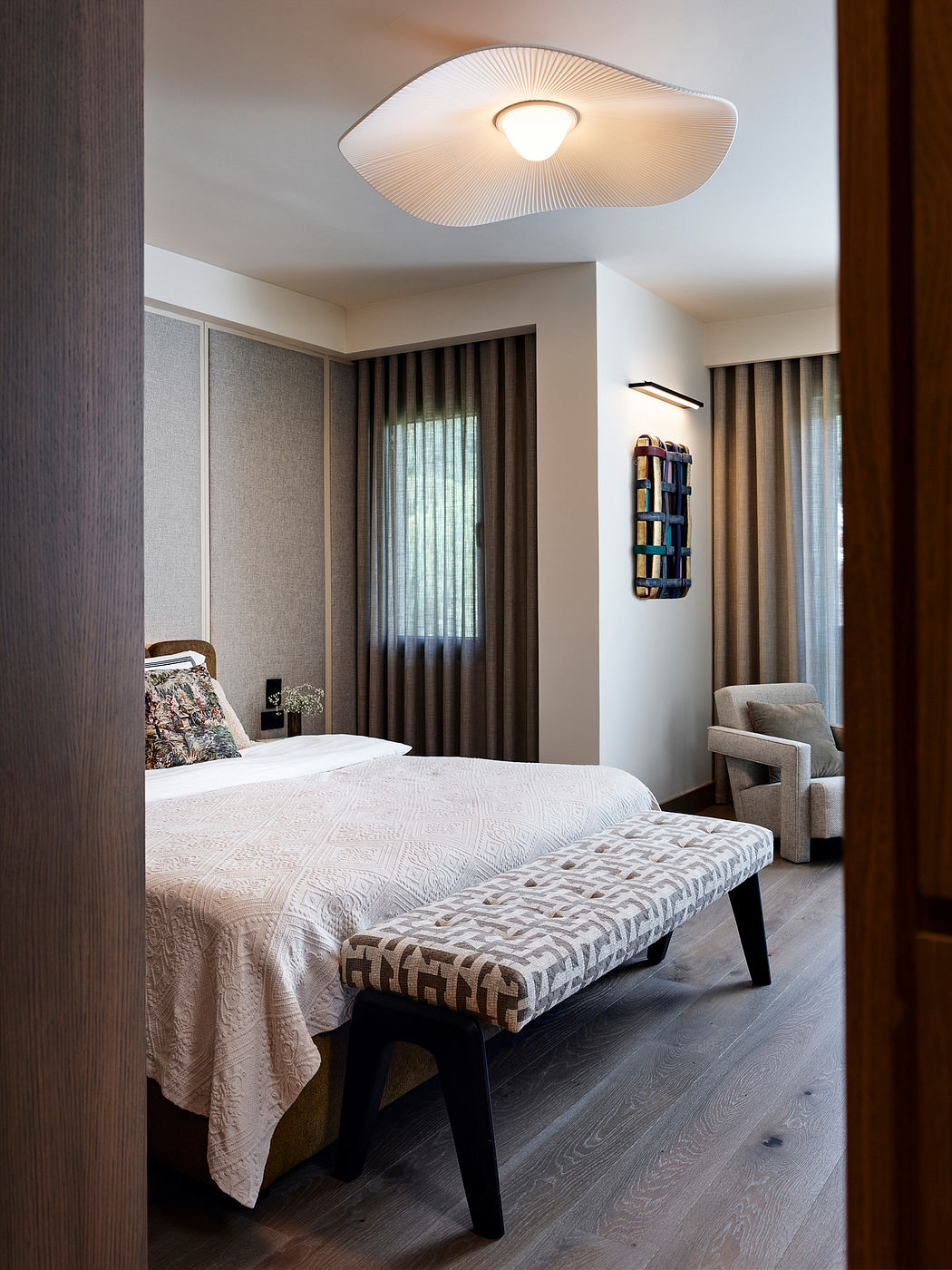 Cozy bedroom with modern curved lighting fixture, textured furnishings, and built-in bookshelves.