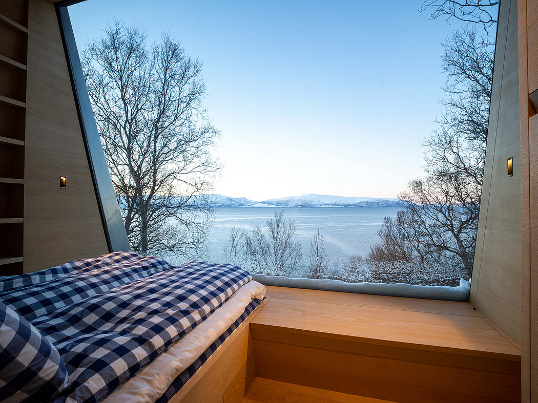 A cozy bedroom with a large window showcasing a scenic lakeside view, nestled among bare trees.
