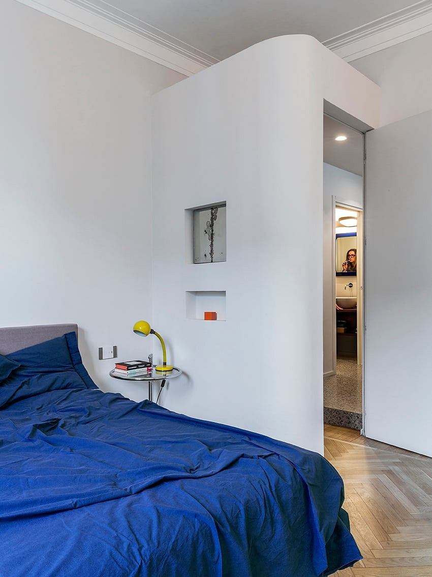 Minimalist bedroom with white walls, floating shelves, and a vibrant blue bedspread.