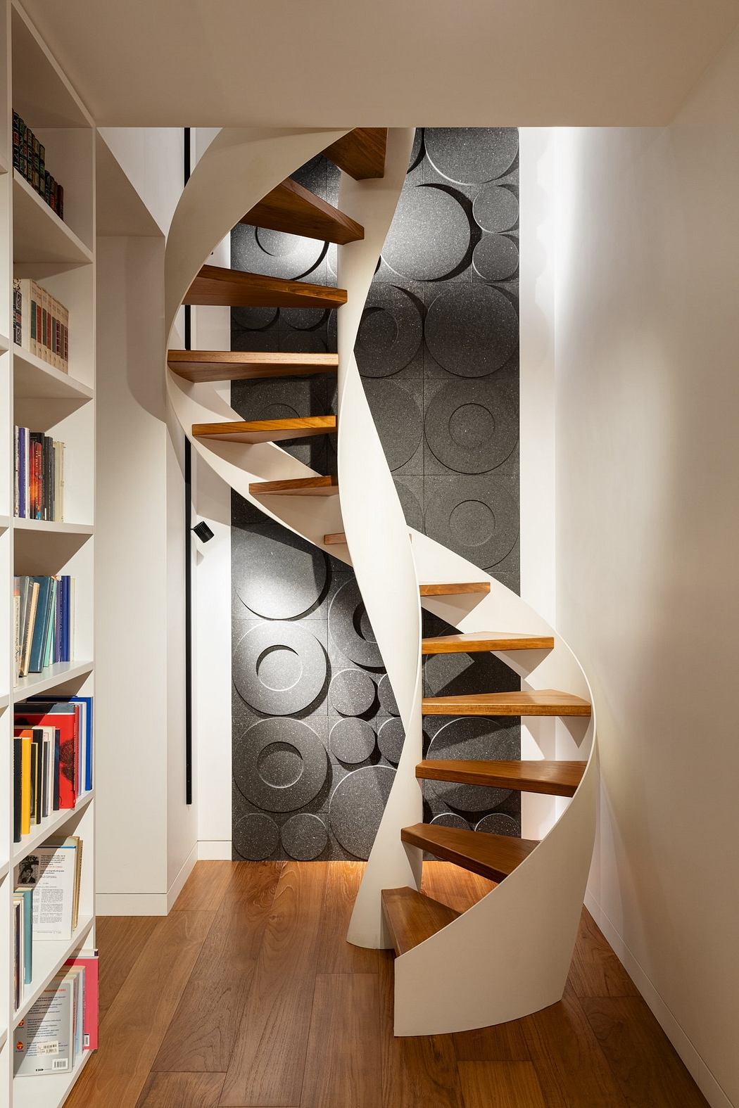 Striking spiral staircase with wooden treads and patterned accent wall in modern interior.