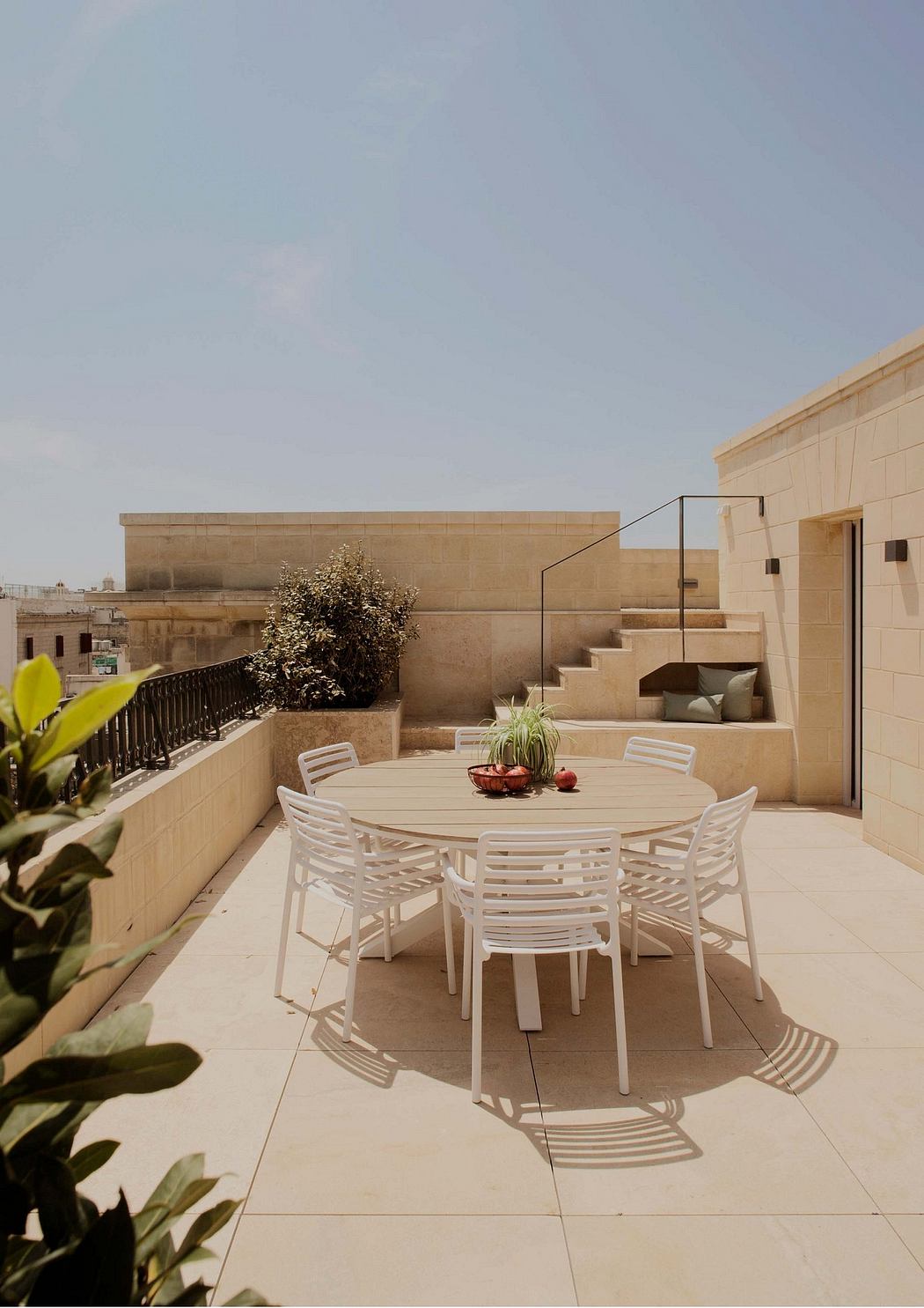 Elegant outdoor dining area with modern white furniture, potted plants, and stairs leading to a raised platform.
