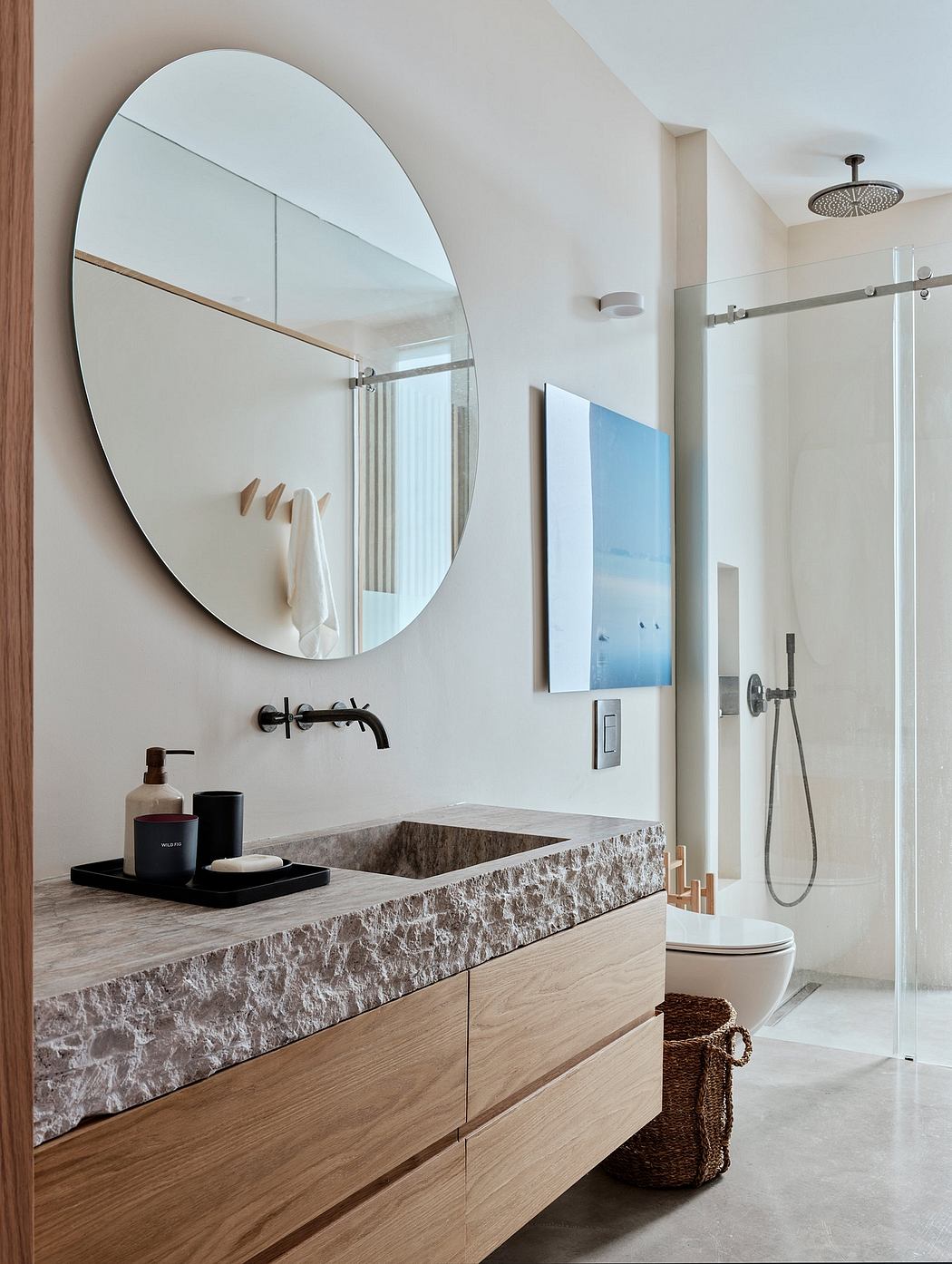 A modern bathroom with a large oval mirror, wood vanity, and sleek shower fixture.