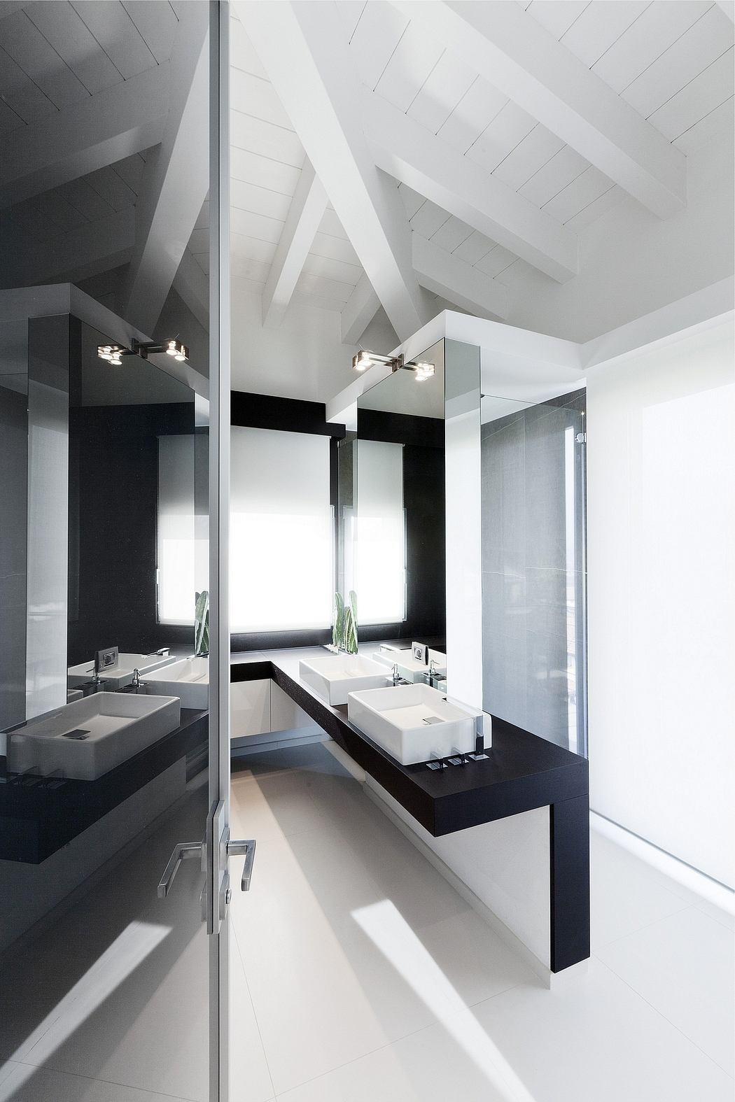 A modern bathroom with sleek black and white design, featuring a vaulted ceiling and dual vanities.