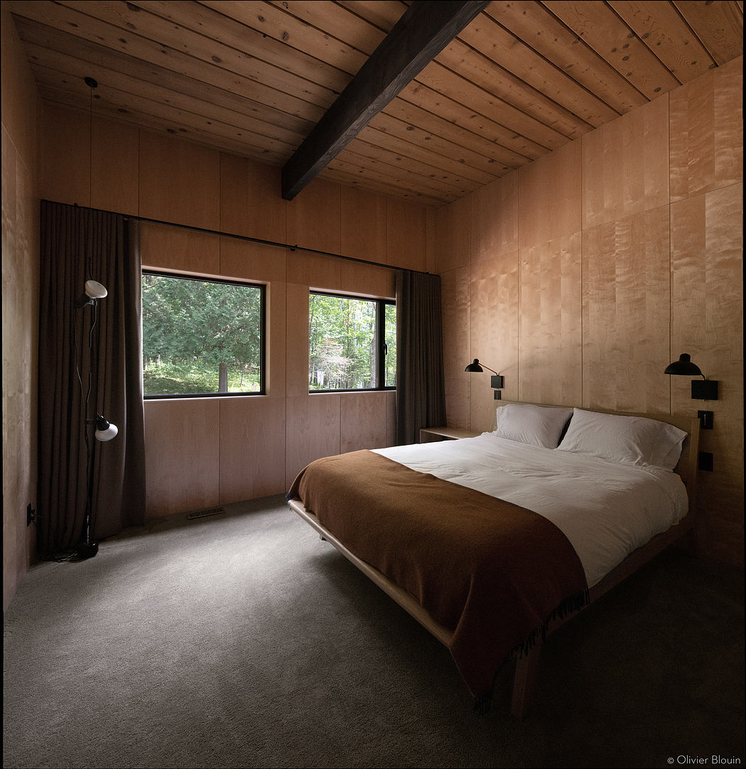 A cozy bedroom with wooden ceiling beams, large windows, and a plush brown bedding.