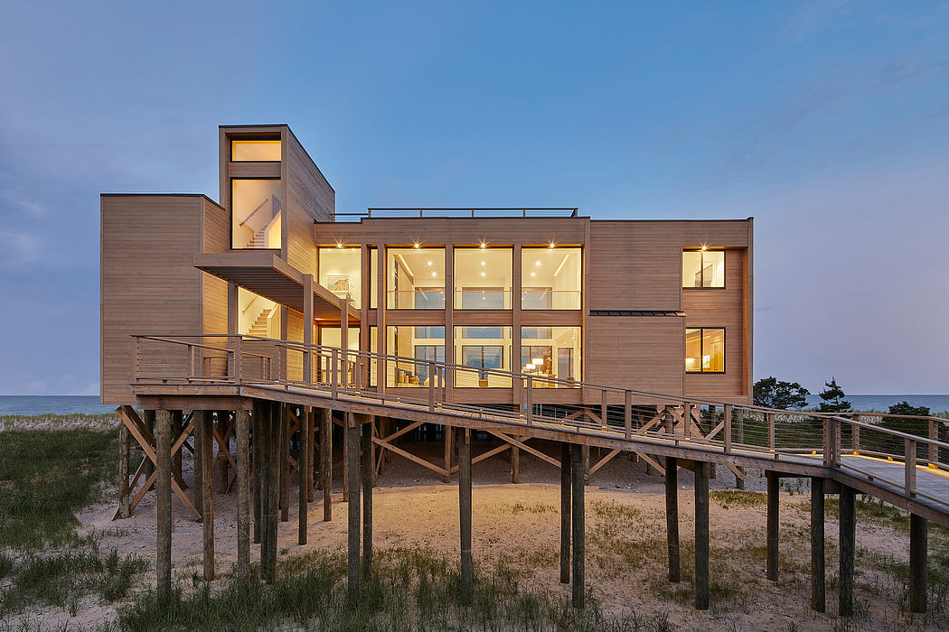 Modern multi-level beachfront house with expansive windows, deck, and wooden supports.