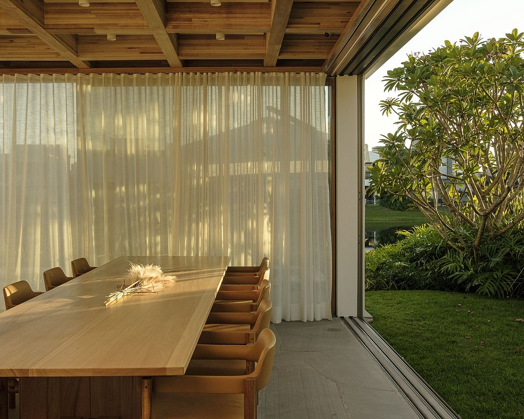 A spacious, minimalist dining area with a wooden table and chairs, surrounded by greenery.