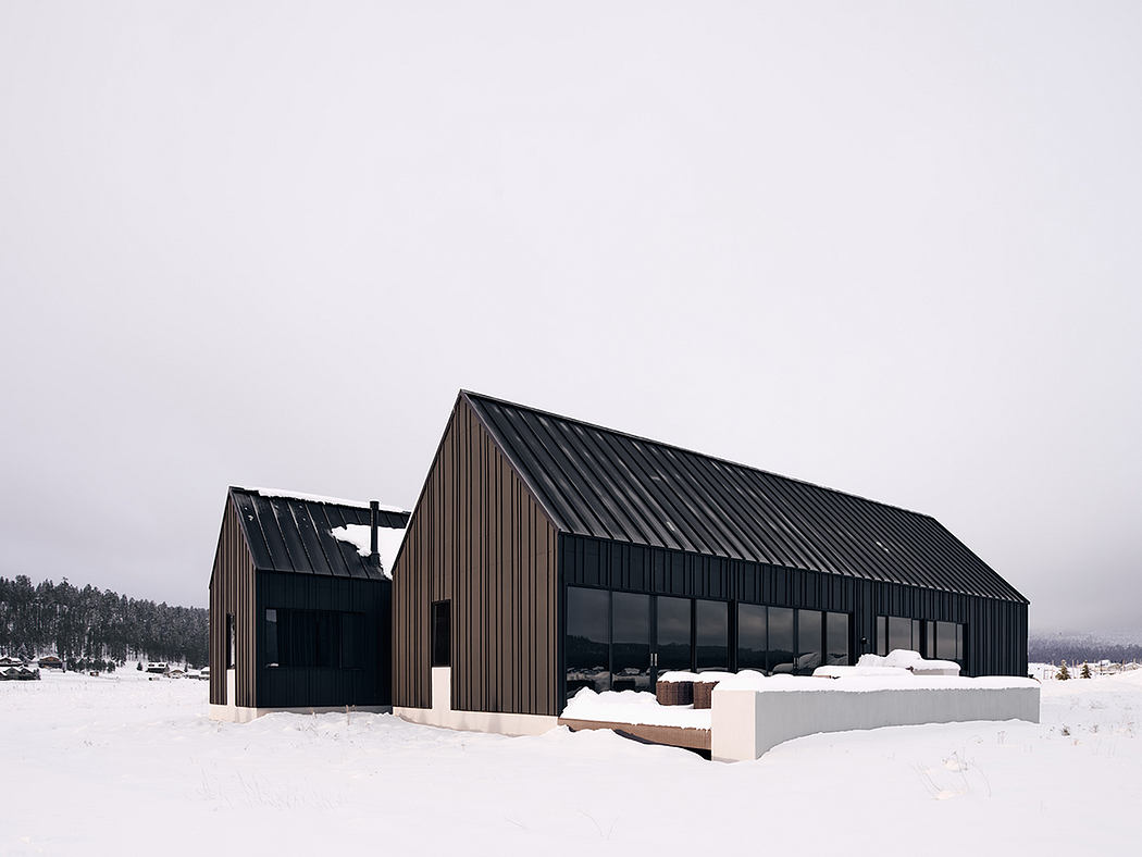 Modern black wooden building with large glass windows against snowy landscape.