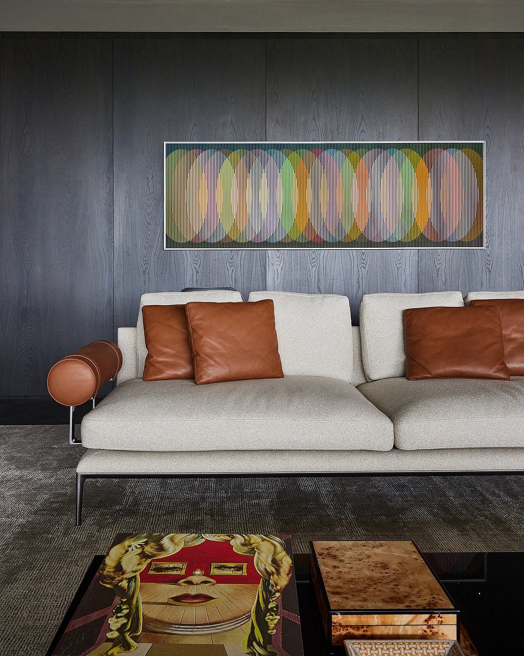 A modern, minimalist living room with a sleek gray couch, leather accents, and a striking abstract artwork.