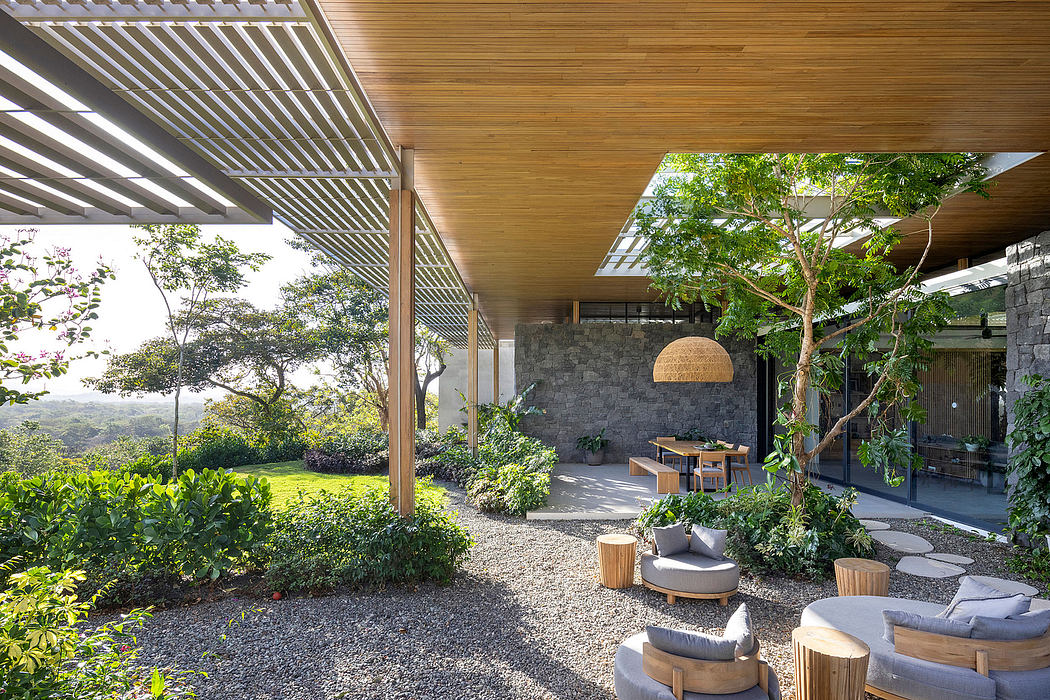 A modern outdoor patio with a wooden pergola, stone walls, and lush vegetation.
