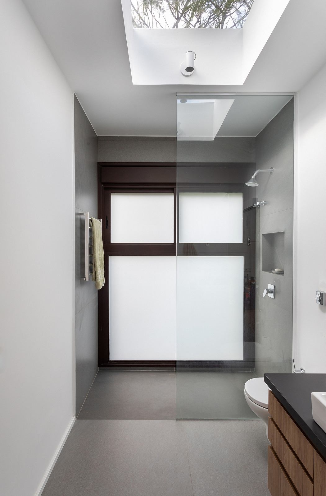 Sleek, minimalist bathroom with large windows, skylights, and a wooden vanity.