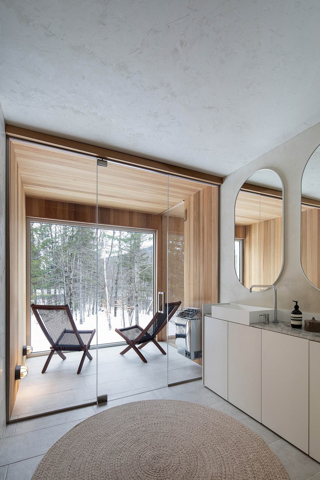 The image showcases a modern, minimalist bathroom with a large window overlooking a wooded landscape.