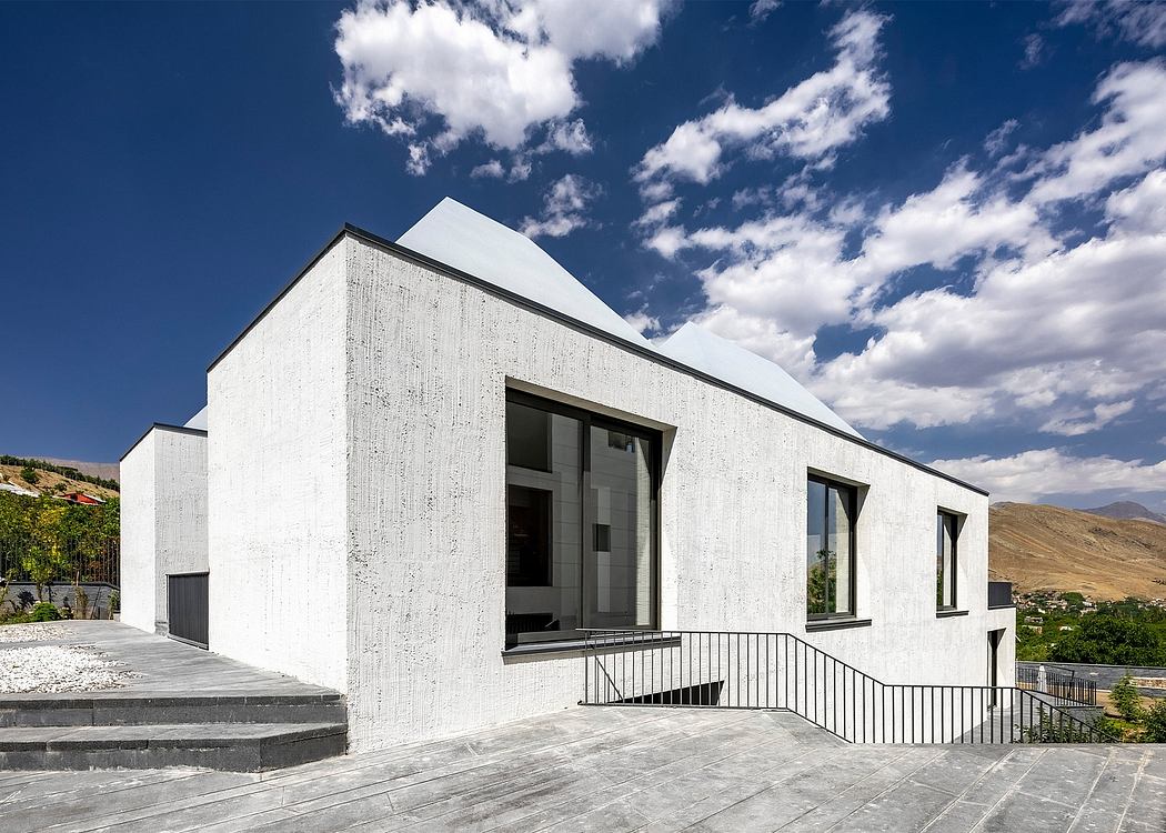 A modern, white concrete building with large windows and a metal railing on the balcony.
