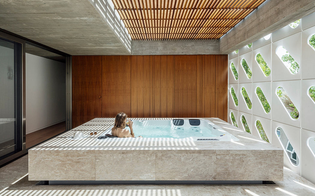 A modern, spa-like interior with a concrete-framed hot tub, wood ceiling, and lush views.