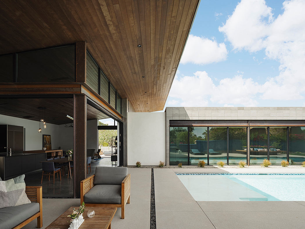 An open-concept living space with a wooden ceiling, large windows, and an outdoor pool visible through the glass.