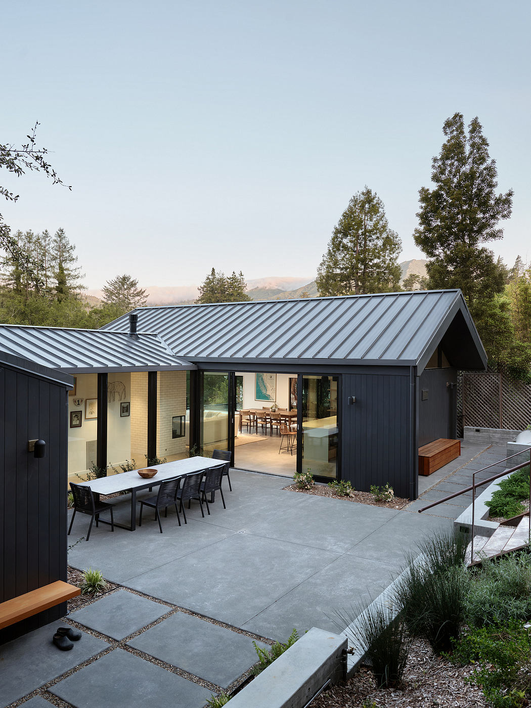 Modern, monochrome home with a sleek metal roof, expansive windows, and a spacious outdoor dining area.