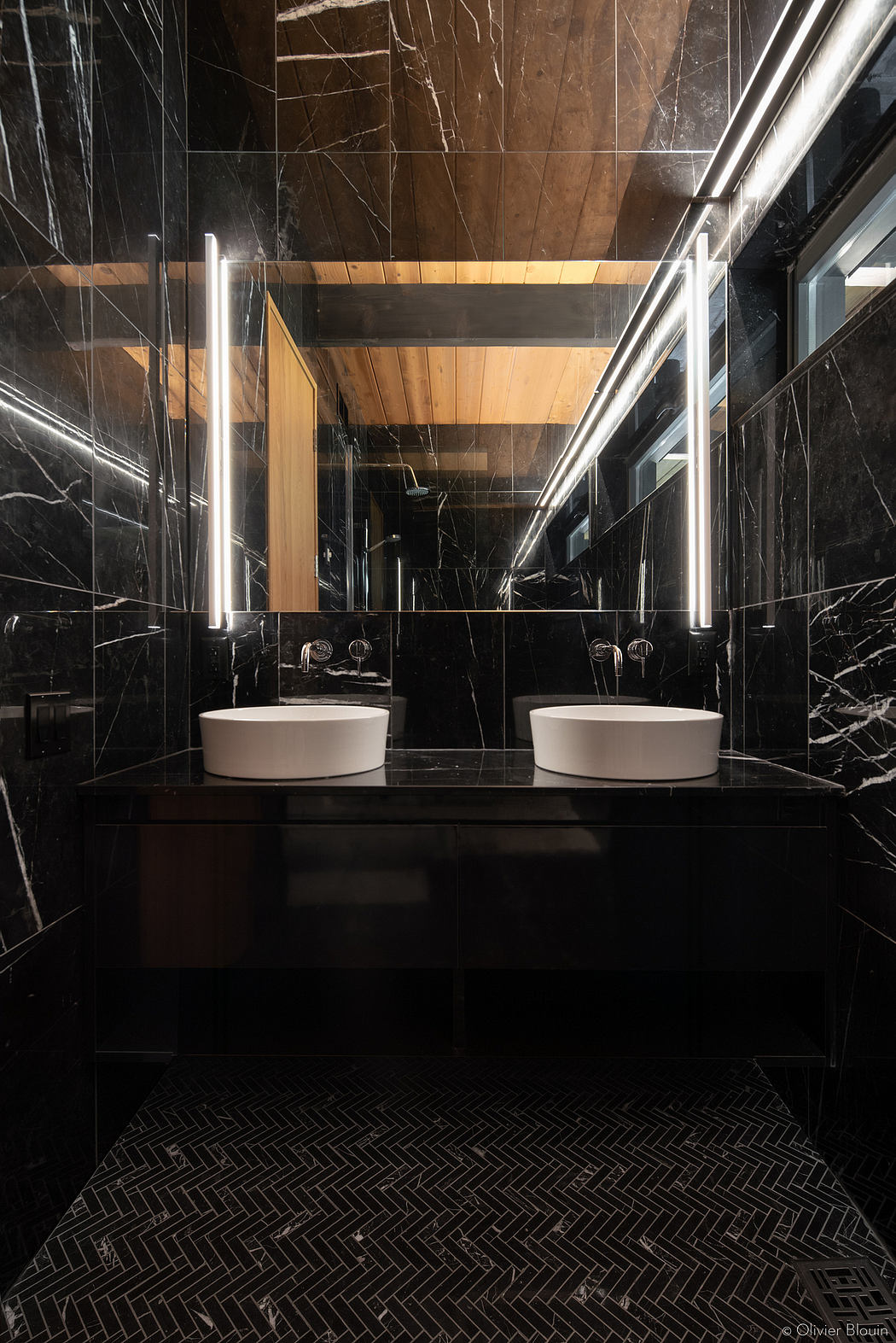 A modern bathroom with sleek black marble walls, wooden accents, and dual vanity sinks.