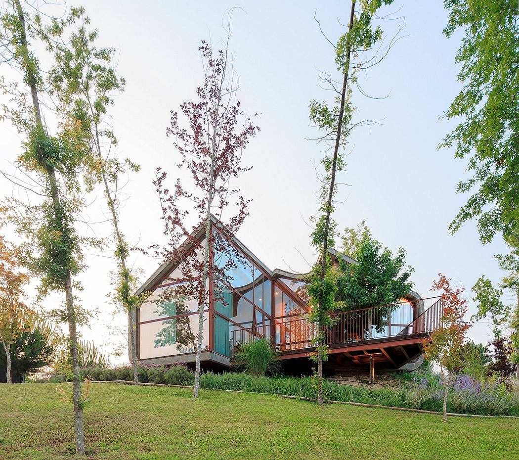 A modern, glass-walled house with a wraparound balcony nestled among lush trees.