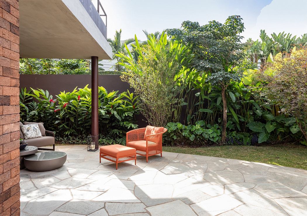 Lush tropical garden surrounds a paved patio with rustic orange seating and a water feature.