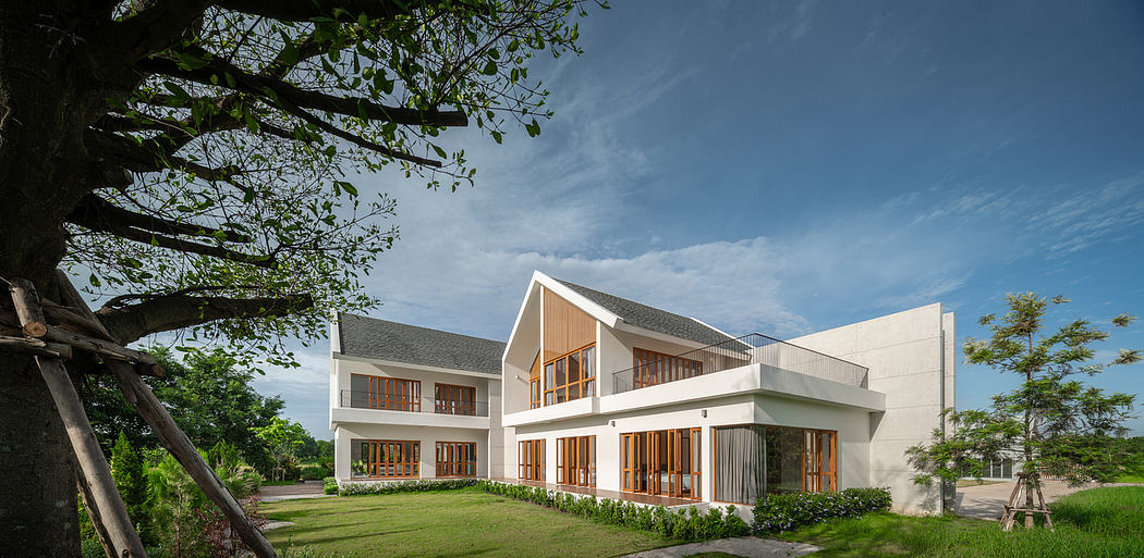 A modern, two-story building with large windows, a slanted roof, and a lush, grassy lawn.