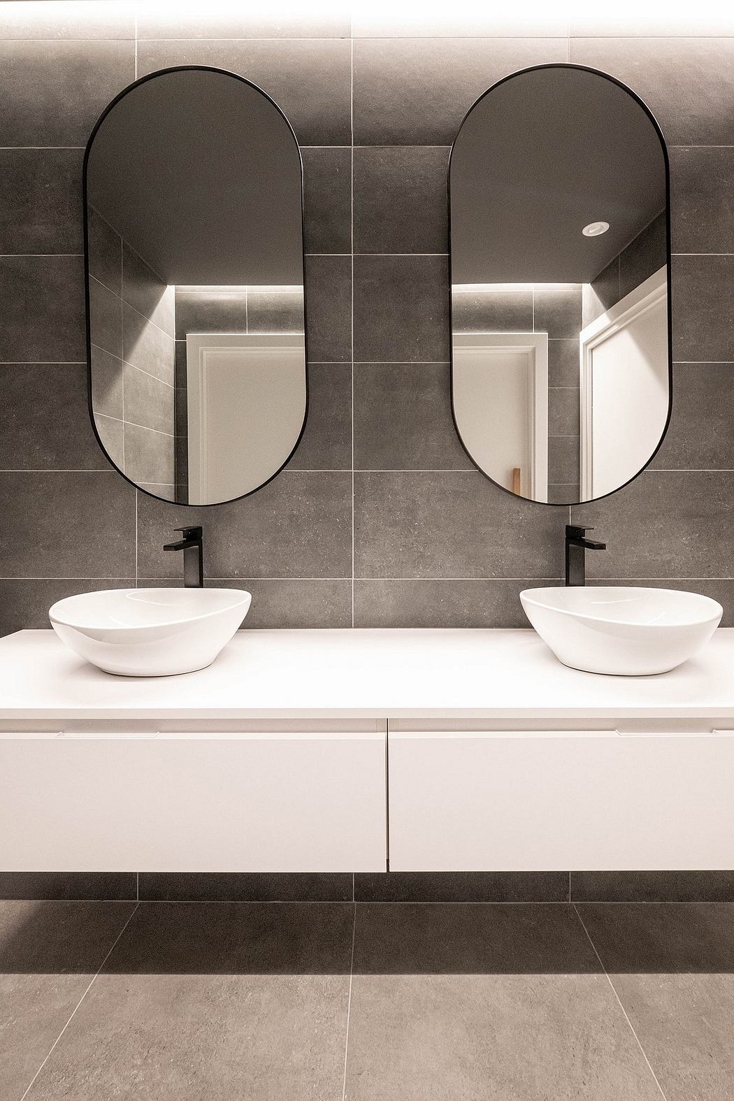 Modern minimalist bathroom with oval mirrors, vessel sinks, and monochrome tiles.