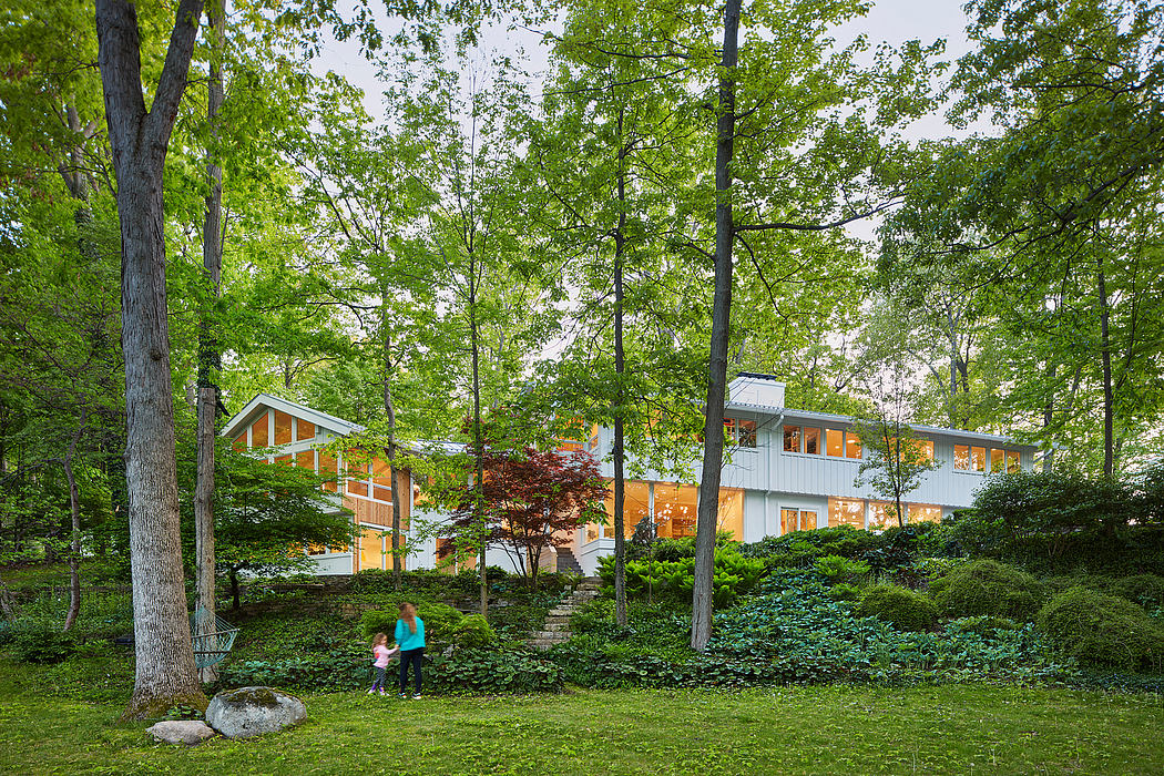 A modern, multilevel house nestled among lush greenery and mature trees, with large windows allowing ample natural light.