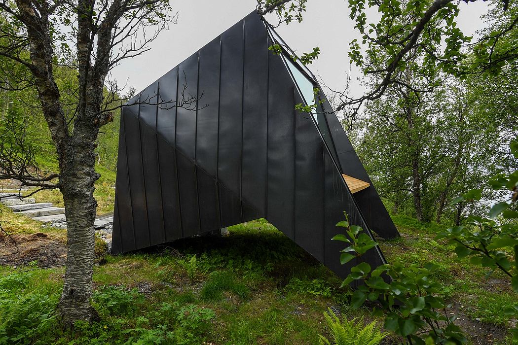 A modern, angular black structure nestled among the lush, verdant foliage.