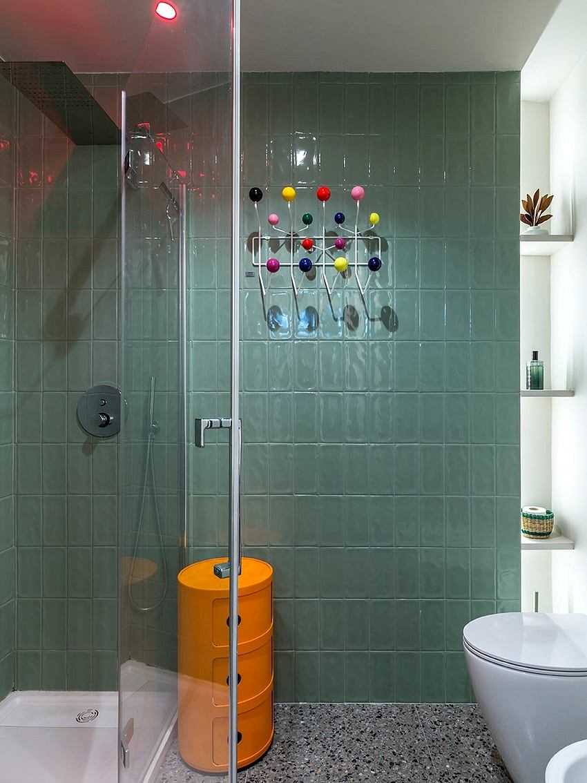 A modern bathroom with vibrant-colored knob accents on green tile walls and orange cylinder.