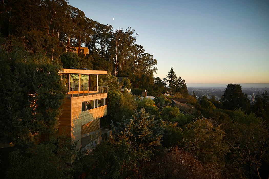 A modern, glass-walled structure nestled in a lush, forested hillside, with a panoramic view of the city.